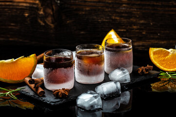 Frozen shot glass alcoholic drinks on rustic wood background. Shot glass of herb liqueur with cinnamon and oranges on a dark background, catering, banner, menu, recipe, place for text © Надія Коваль