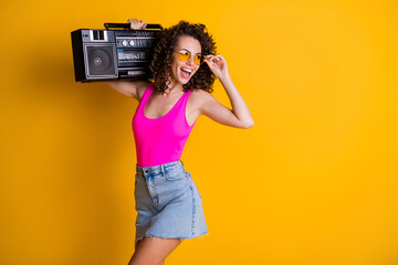 Photo of cool youngster lady wavy hairdo listen music hold retro boom box chill beach pool students party wear sun specs pink singlet denim skirt isolated vibrant yellow color background