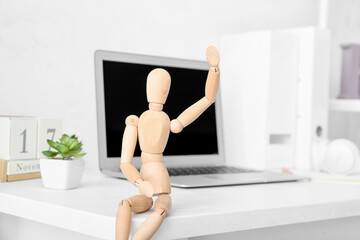 Wooden mannequin with laptop on table in office