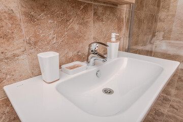 Close up of a snow-white sink in a cozy tiled bathroom in light colors. White bathroom accessories