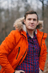 Portrait of young man in orange jacket walking in autumn forest. Adult male posing on fresh air in autumn season.