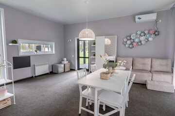 Spacious bright hotel room with modern matte interior and decor. White dining table, soft light sofa, mirror cabinet, wall decorations and full carpet