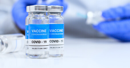 Coronavirus vaccine vials on a white plate with copyspace. Doctor or nurse taking medicine with a syringe in the background