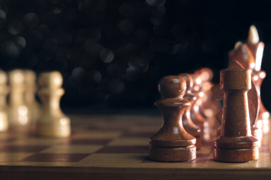 Wooden chess pieces and a chessboard on blurred dark background, selective focus