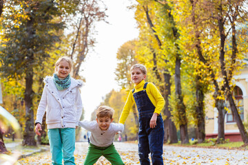Fototapeta premium Children girl and two boys playing with soap bubbles, someone blows children catch bubbles. Beautiful natural landscape, autumn park on background, happy childhood.
