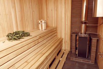 Fototapeta na wymiar Spacious wooden sauna with a beautiful brick stove and a birch broom on a bench