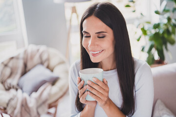 Photo of dreamy attractive young woman smell coffee in cup closed eyes enjoy weekend in home indoors
