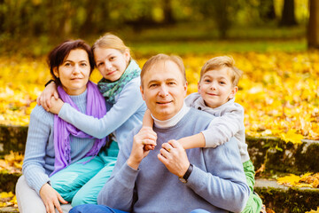 Happy family of four having fun time at autumn park together. Mother, father and two children sitting and hugging together outdoor during holiday.