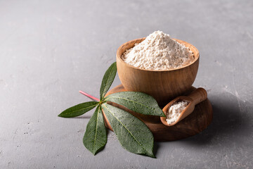 Cassava (manioc) flour in wooden bowl with original leaf on grey background.