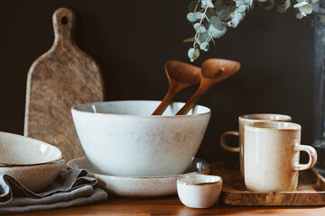 Set of kitchen ceramic tableware and wooden cutting boards on a table. Eco style home still life.