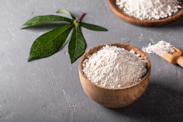 Cassava flour in wooden bowl with original leaf on grey background.