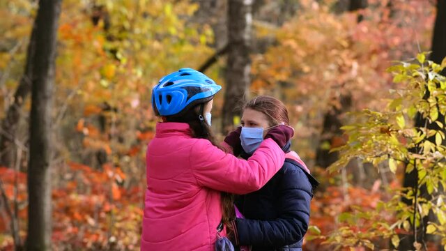 The older sister puts on the younger one a medical mask and a Bicycle safety helmet in the fall . The concept of protection FROM covid-19 coronavirus infections.