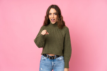 Young woman over isolated pink background surprised and pointing front