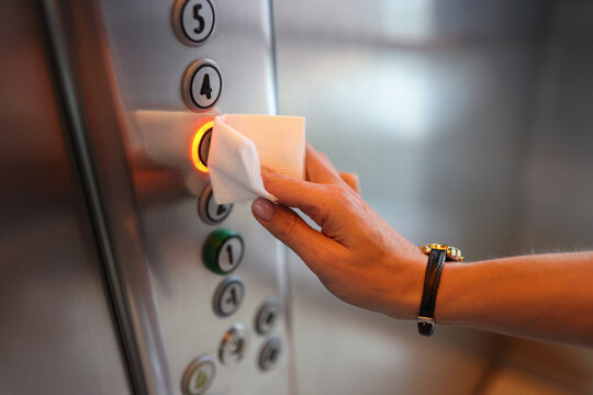Female hand presses button in elevator through napkin. Use of items in the coronavirus pandemic concept