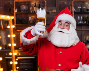 Santa claus with a glass of light beer wishes merry christmas and says toast