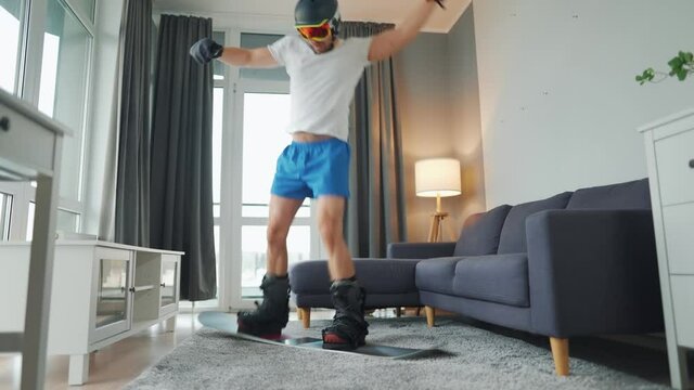 Fun video. Man in shorts, t-shirt and snowboarding equipment happily dancing and having fun on a carpet in a cozy room. Waiting for a snowy winter