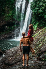 A man holds a woman in his arms at the waterfall. Couple at the waterfall, rear view. Honeymoon trip. Happy couple on vacation in Bali. A couple in love travels the world. Copy space