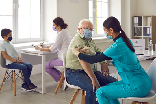 Doctor And Nurse In Medical Uniform And Protective Masks Making Vaccination Against Covid-19 Virus