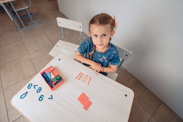 Top view of a cute pretty attractive female kid sitting at a white table where logic puzzles are...