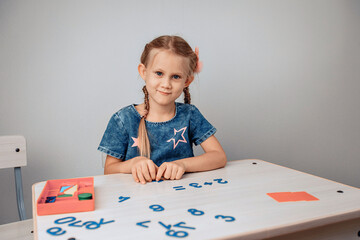 Portrait of a pretty smiling lovelylittle child sitting at a white table and studying numbers. Knowledges concept. photo with noise