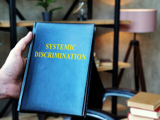 Lawyer holds Systemic Discrimination book in the office.