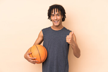 Young african american man isolated on beige background playing basketball and with thumb up