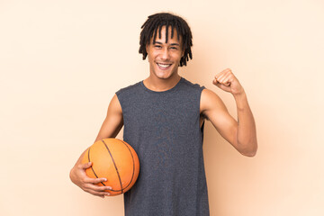 Young african american man isolated on beige background playing basketball and proud of himself