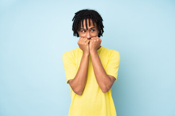 Young african american man isolated on blue background nervous and scared putting hands to mouth