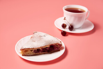 piece of cherry pie on a plate with tea in a white mug. pink background