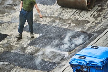 worker man walks on new smoking asphalt