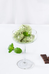 Scoops of mint ice cream with chocolate crumbs in a glass over white background.