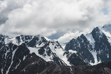 Atmospheric minimalist alpine landscape with massive hanging glacier on big mountain under cloudy sky. Cracks on ice. Low clouds over snowbound huge mountain range. Majestic scenery on high altitude.