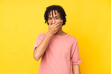 Young african american man isolated on yellow background covering mouth with hands