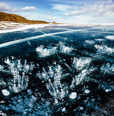 Cracks and bubbles on the surface of the ice frozen lake. Lake Baikal in winter,  clear smooth ice near rocky shore.