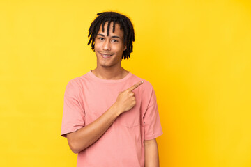 Young african american man isolated on yellow background pointing to the side to present a product