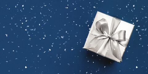 Silver gift box with bow on blue background. Flat lay, top view. Banner with copy space for text.