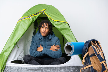Young african american man inside a camping green tent looking up while smiling