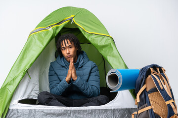 Fototapeta na wymiar Young african american man inside a camping green tent keeps palm together. Person asks for something