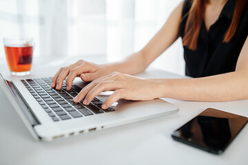 Fototapeta na wymiar Close-up image of female entrepreneur working on laptop at office desk and drinking black tea