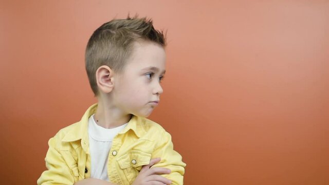 Studio portrait of naughty kid pouting lips, feeling offended, turning away from camera, orange studio background