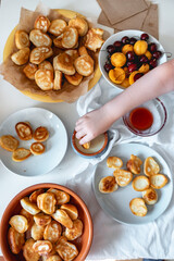 Delicious breakfast with tiny mini pancakes, cherries, apricots, jam on a white table. Small children hold pancakes in their hands. view from above