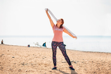 Adult happy woman in sports clothes, posing with a towel on the background of the sea and the beach. Copy space. The concept of sport and activity