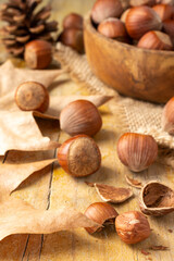 Close-up of wooden bowl with hazelnuts on burlap cloth, with leaves and autumn motifs on rustic wooden table, vertical
