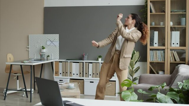 Lockdown of joyful Caucasian female manager wearing smart casual clothes dancing in the office