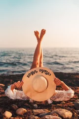 Sommerferien. Eine Frau mit Strohhut liegt mit erhobenen Beinen am Strand, am Strand. Rückansicht. Platz kopieren © _KUBE_