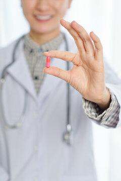 Smiling doctor showing bright pink pill that can relieve severe pain