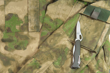 a folding knife lies on a military camouflage jacket