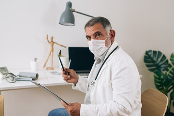 doctor with protective face mask sitting in his office