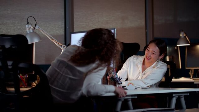 Young Professional Women Talking and Smiling While Working Late in Office
