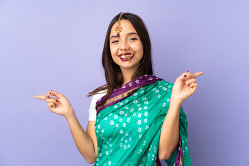 Young Indian woman isolated on purple background pointing finger to the laterals and happy